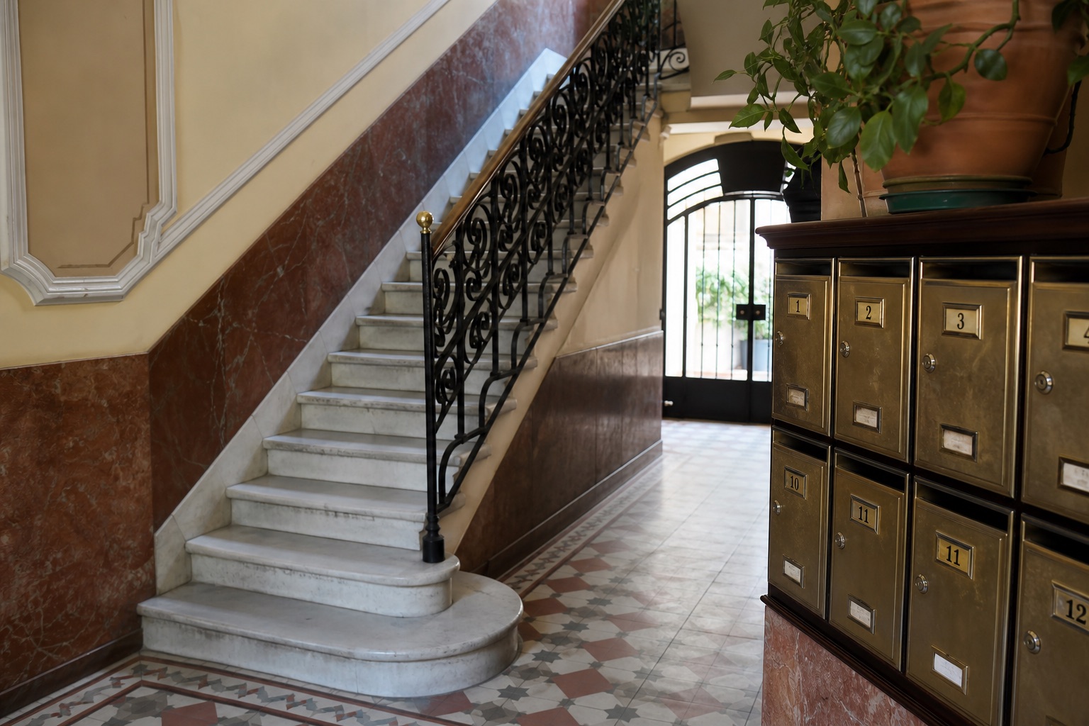 Vestíbulo de un edificio de viviendas tradicional español con buzones numerados de latón, escalera de mármol con barandilla de hierro y suelo de baldosa hidráulica