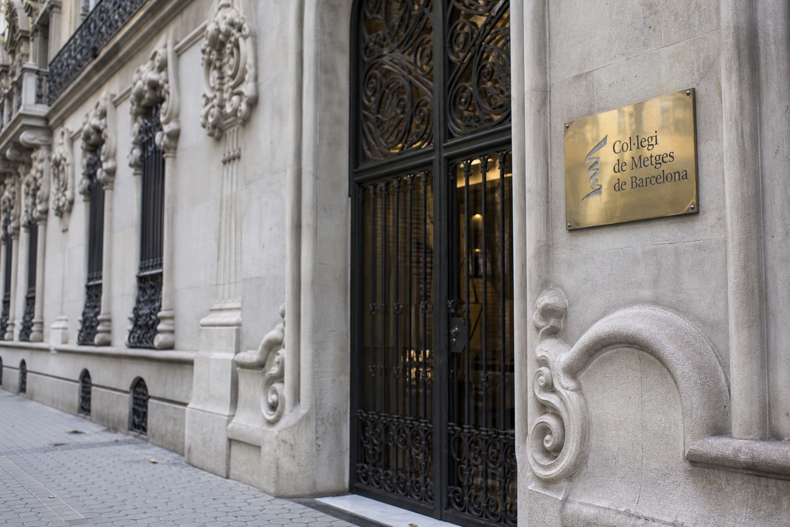 Fachada de un edificio oficial modernista de Barcelona con detalles de piedra y una pequeña placa de latón junto a la puerta de entrada