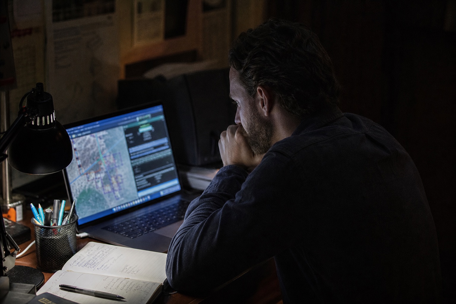 Portátil con mapas y datos junto a un cuaderno de anotaciones, en un puesto de análisis nocturno